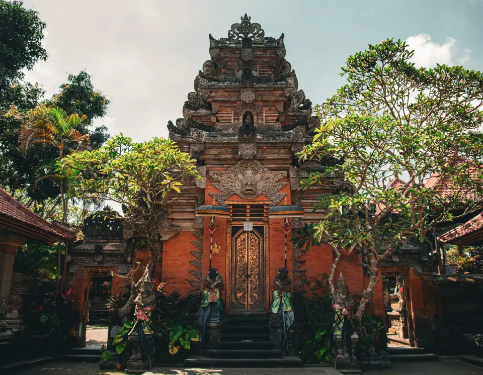 A carved split gateway of a Balinese temple framed by frangipani trees