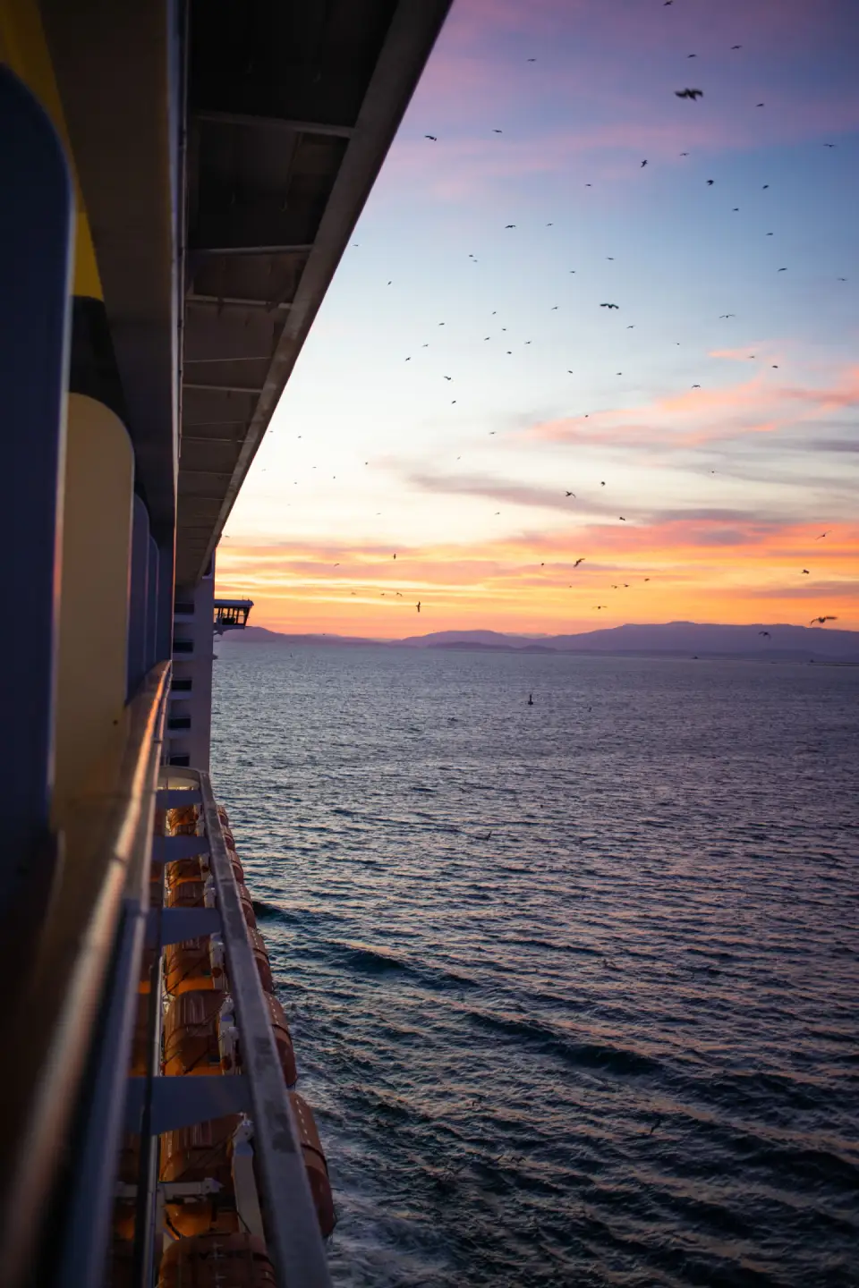 Sunset over the sea seen along the side of a cruise ship from a balcony