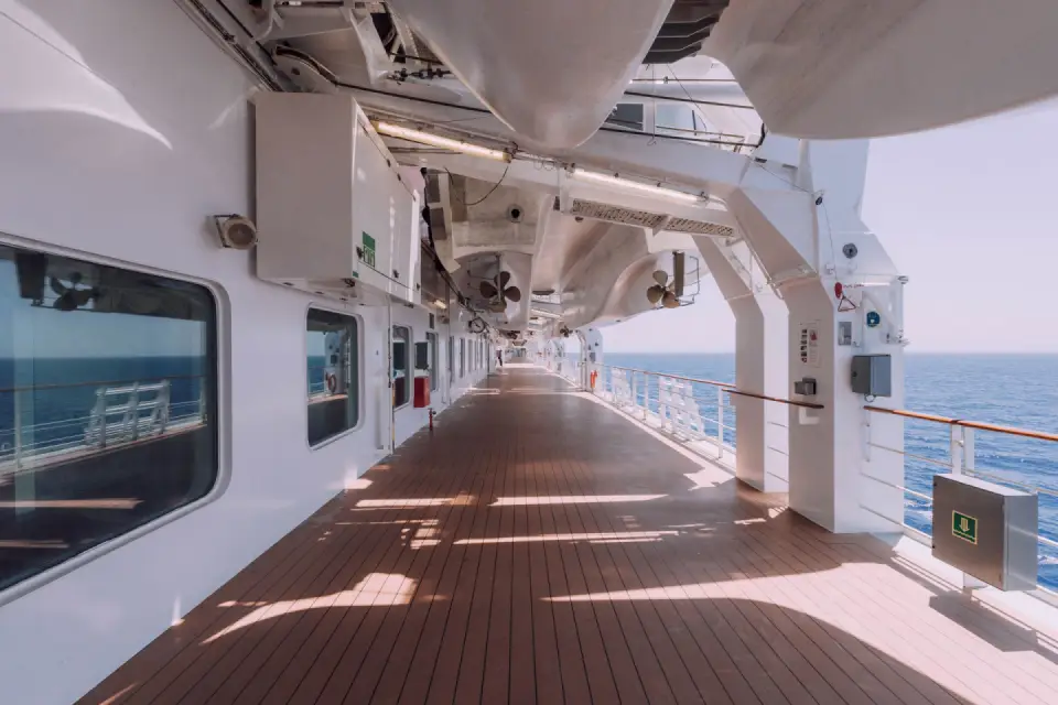 Long sunny promenade deck under lifeboats with the open sea alongside