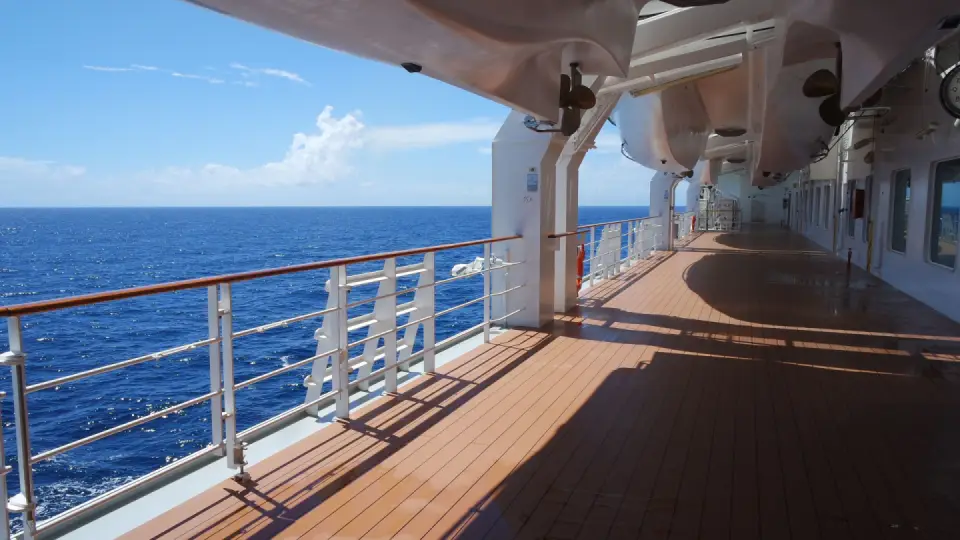 Sunlit wooden promenade deck beside deep blue open ocean