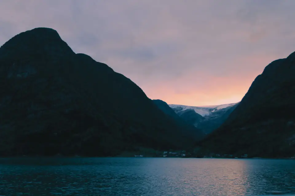 Steep mountains framing a fjord at sunset with a glacier in the distance
