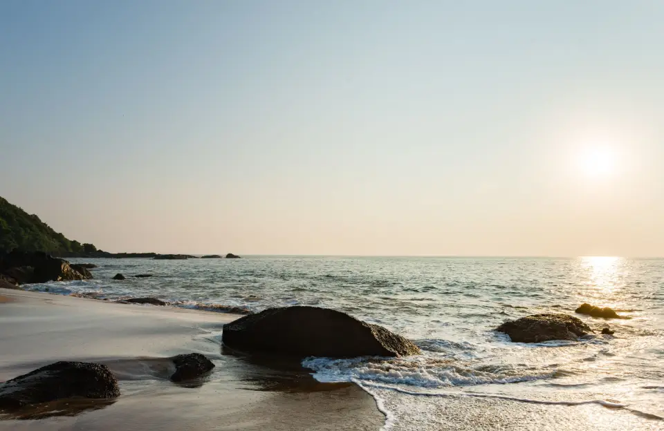 The sun setting over rocks and surf on the Goa coast