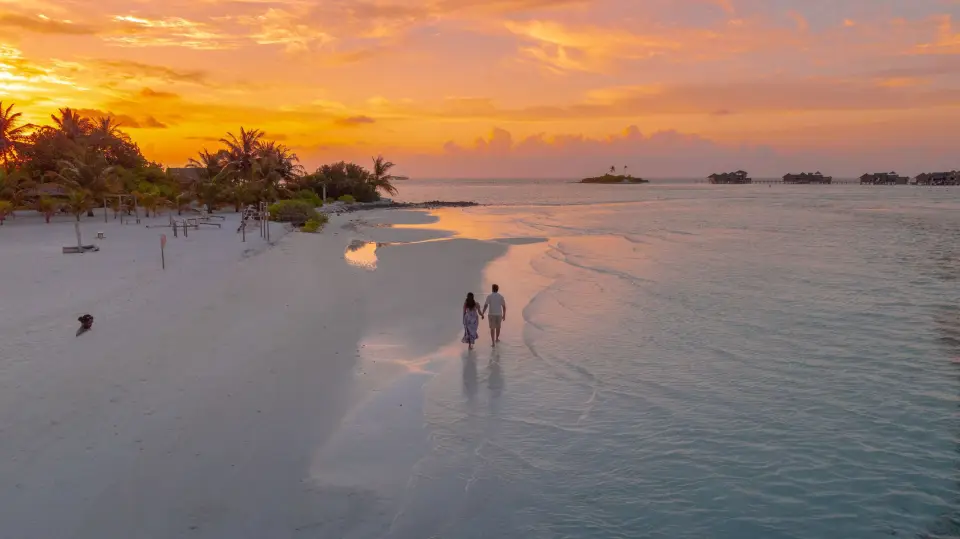 A couple walking along a Maldives sandbank at sunset